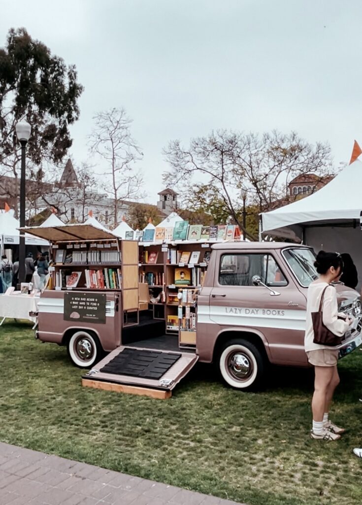 Image of a dusty rose 1961 Chevy Rampside that's been customized into a book store and reads, Lazy Day Books on it's side