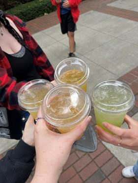 Hands of four people brining their aqua fresca's together for a "cheers!" outside at the Festival of Books. The lighting is a bit gloomy.